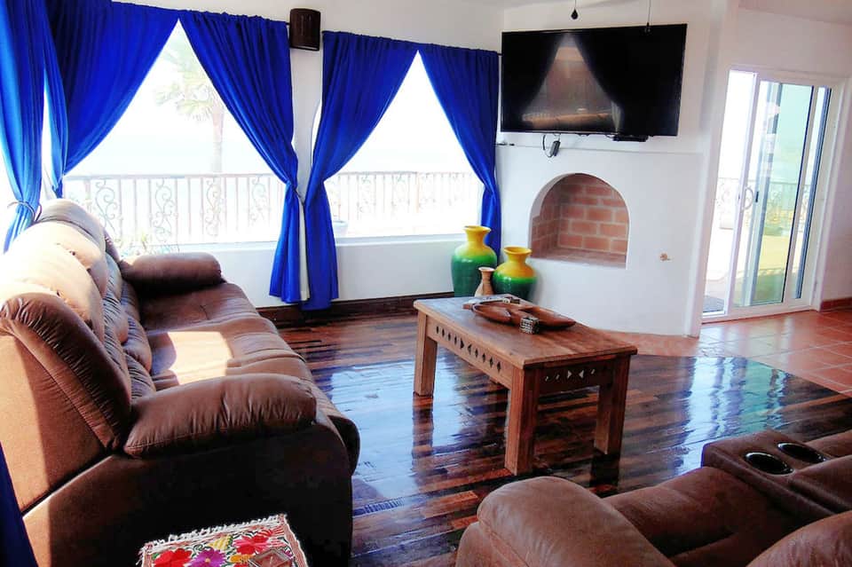 Spacious living room with brown leather furniture, fireplace, blue curtains, and ocean view balcony