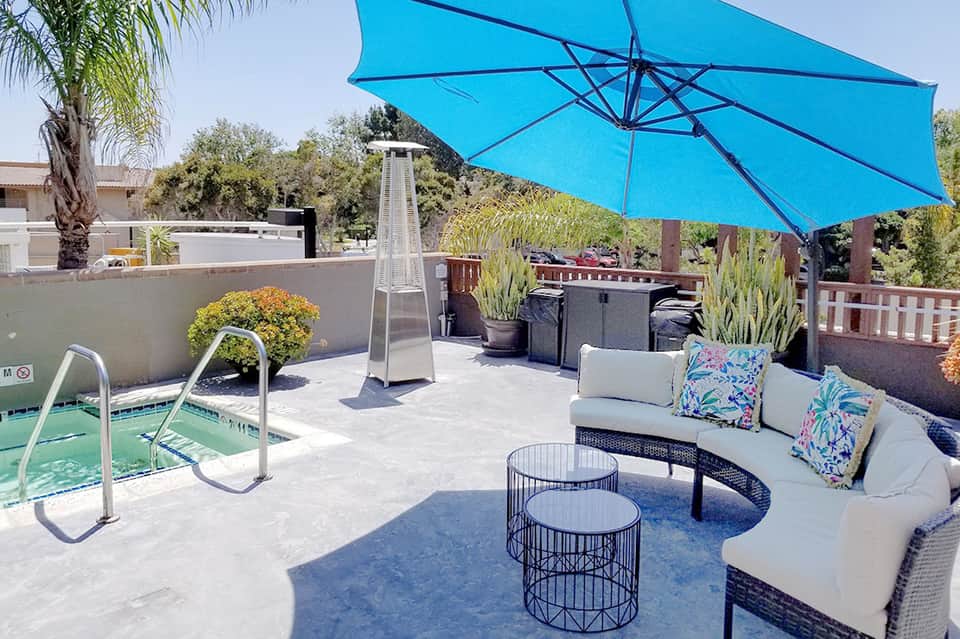 Modern rooftop patio with blue cantilever umbrella, lounge seating, heater, and manicured plants