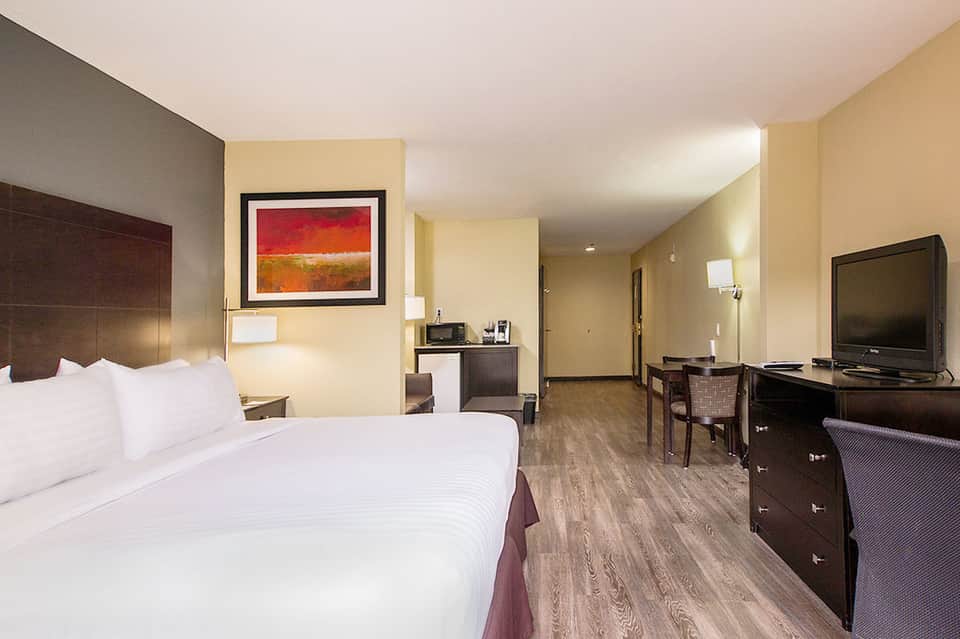 Modern hotel bedroom with queen bed, desk area, and flat-screen television