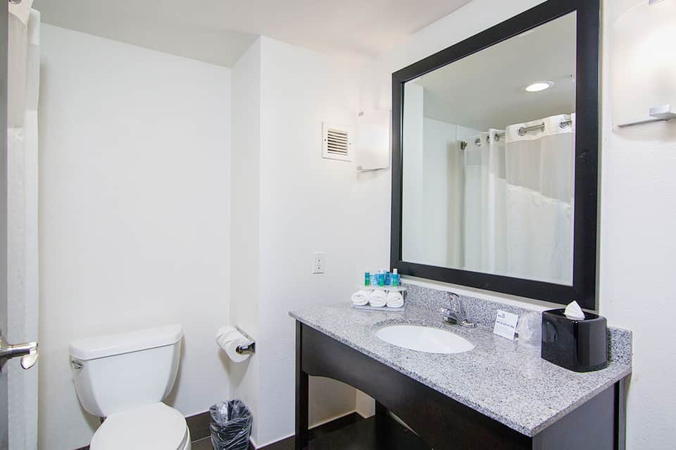 Clean bathroom vanity with gray countertop, large mirror with black frame, and white toilet