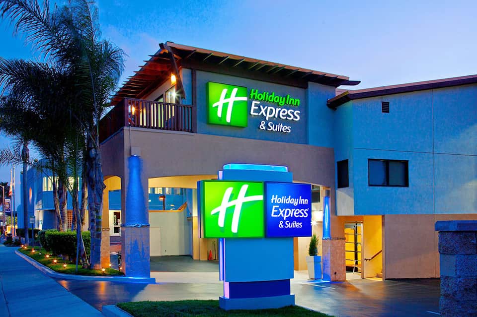 Holiday Inn Express & Suites exterior at dusk with blue, yellow signage and palm tree landscaping