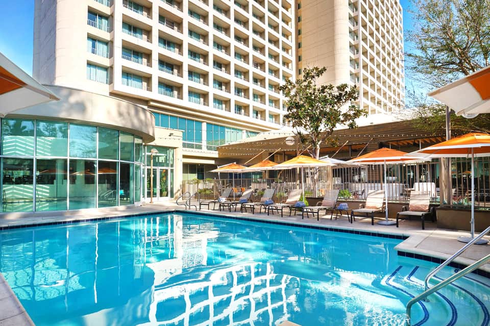 Resort pool with orange umbrellas, lounge chairs, and modern hotel building in daylight
