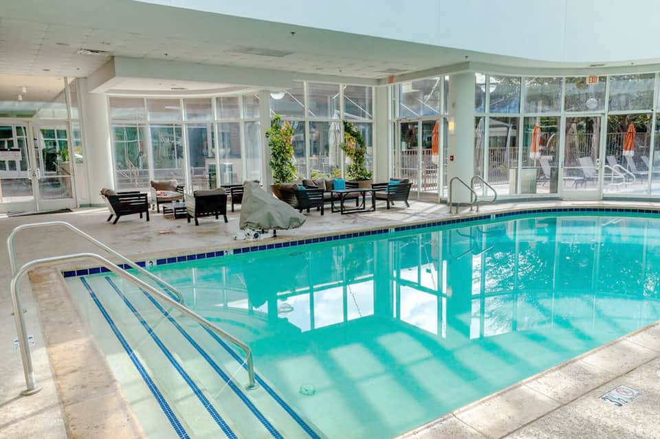 Indoor swimming pool with lane markings, surrounded by large windows and lounge seating area