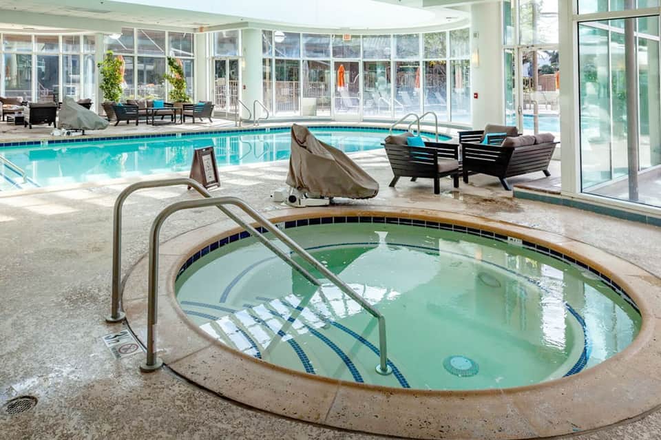 Indoor pool facility with spa hot tub, loungers, and large window walls