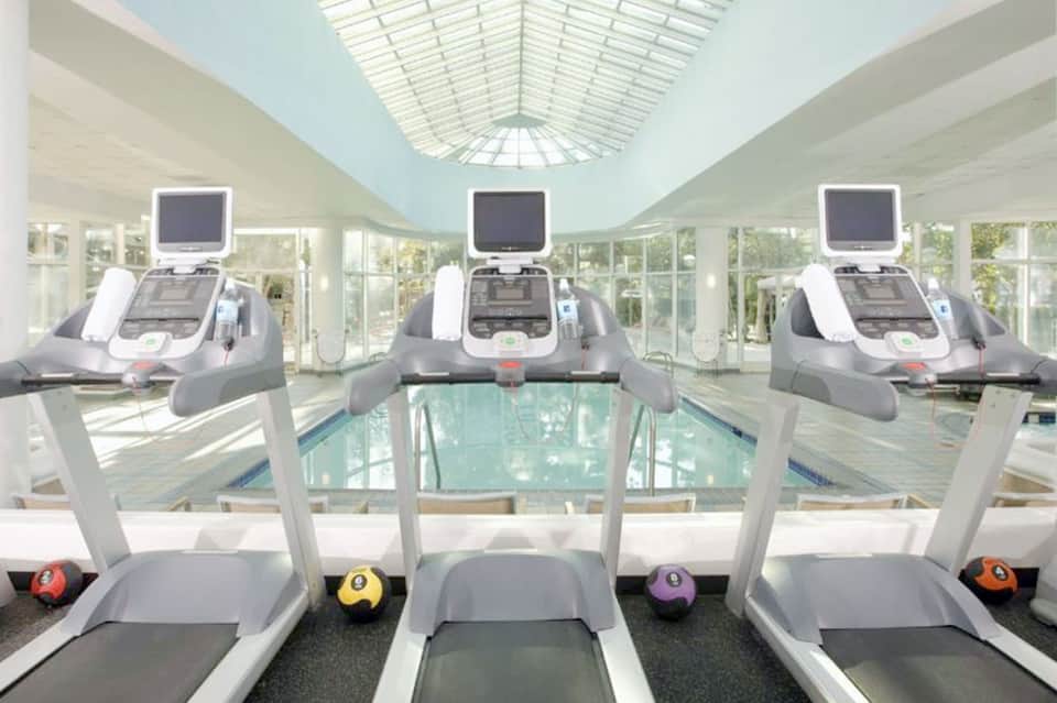 Gym interior with three treadmills overlooking an indoor swimming pool