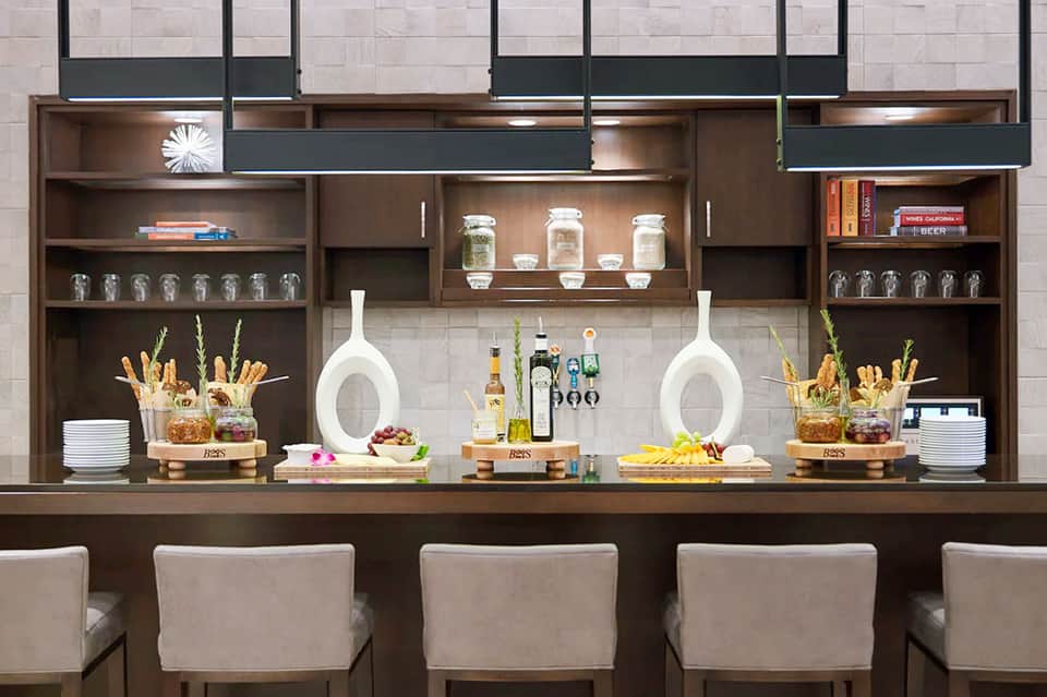 Modern bar counter with shelving, bottles, white bottles, and upholstered seating