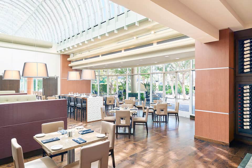 Contemporary restaurant interior with open kitchen, warm wood tones, and large windows