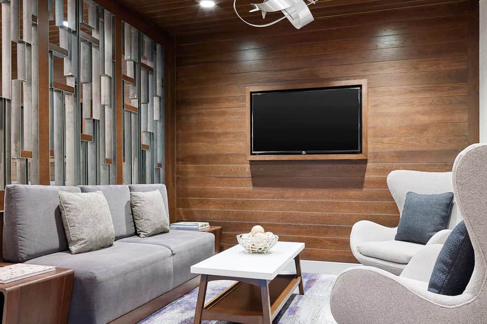 Modern home theater room with wood paneling, gray sofa, and mounted flat-screen TV