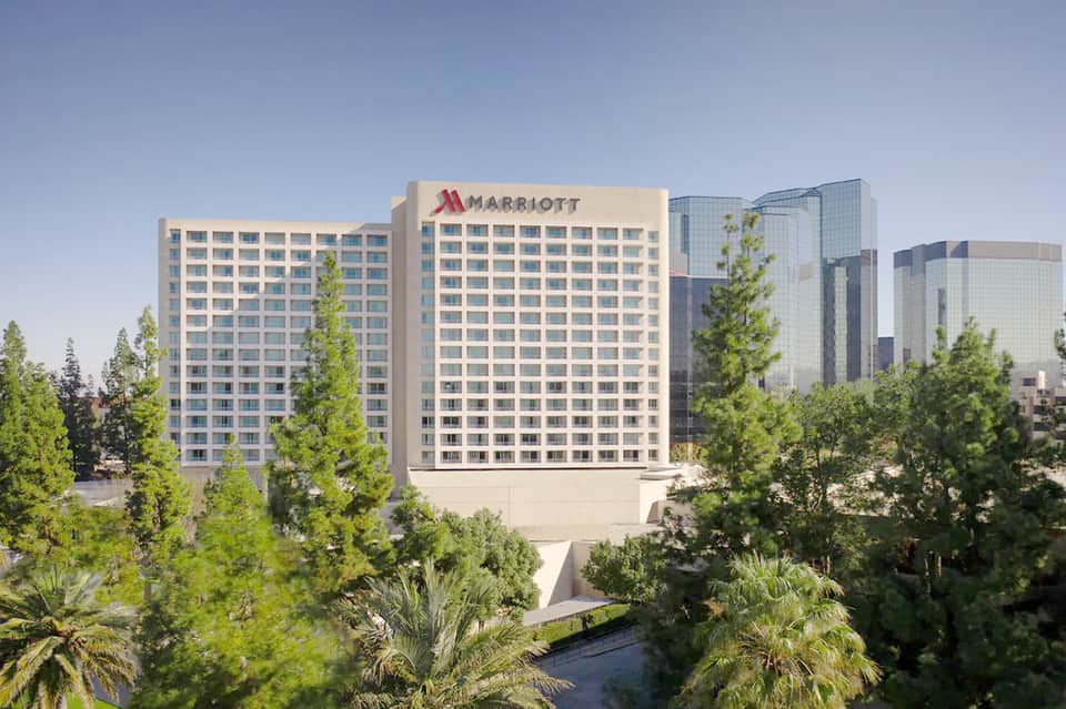 Multi-story Marriott hotel building with glass tower and surrounding palm trees in daytime
