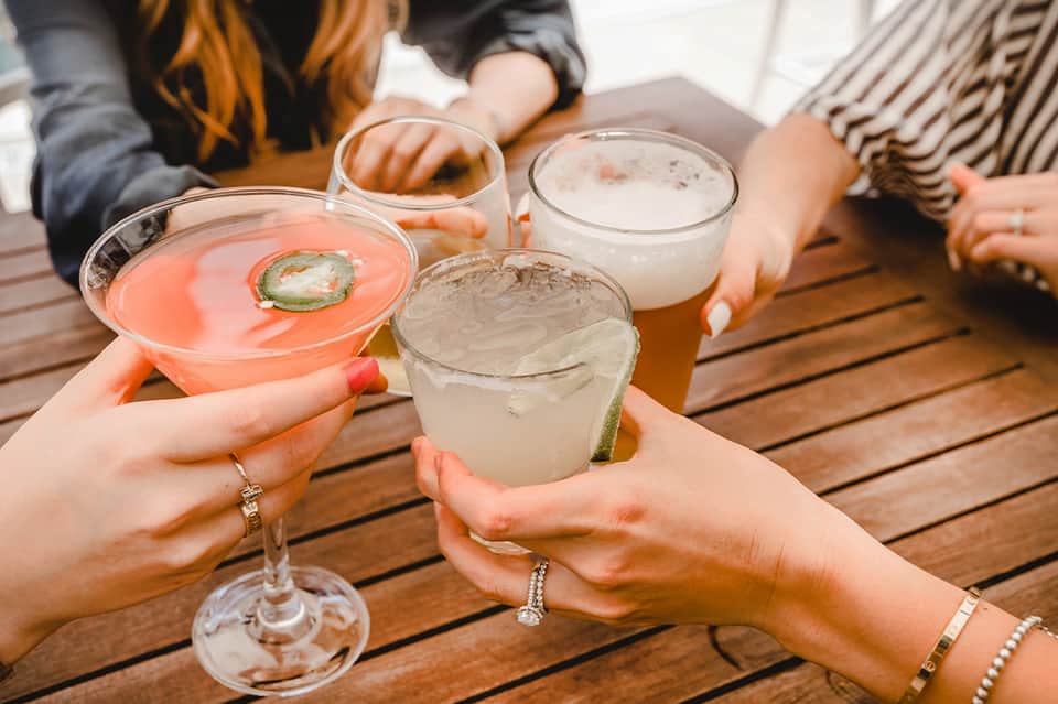 Group holding colorful cocktails on wooden deck during outdoor gathering