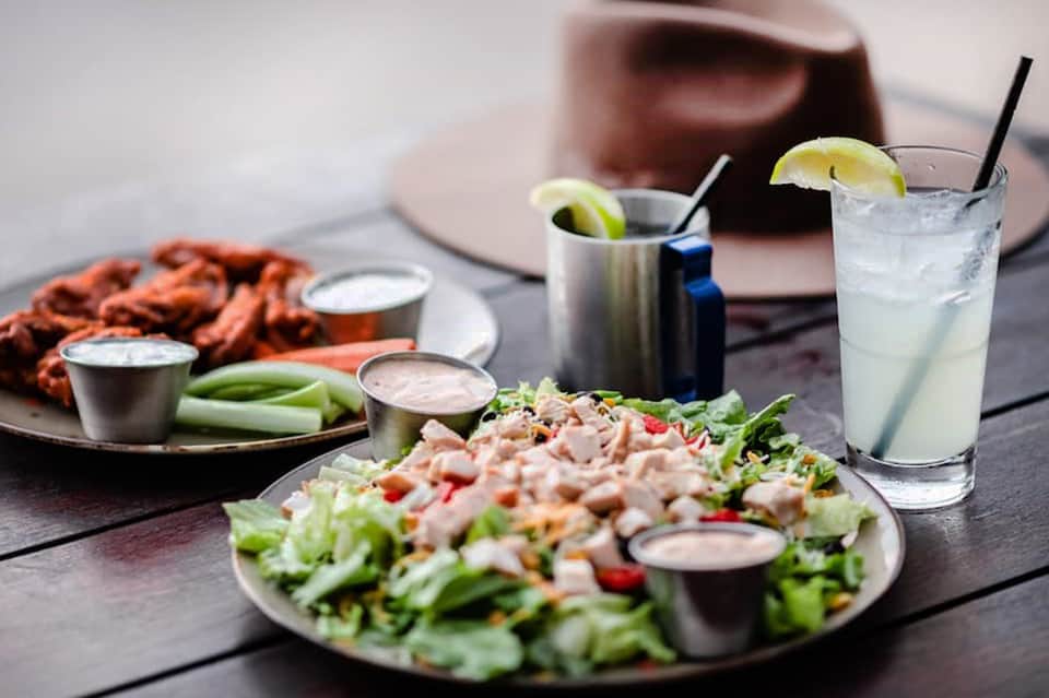 Outdoor dining table with salads, cocktails with lime, and snacks on a wooden deck