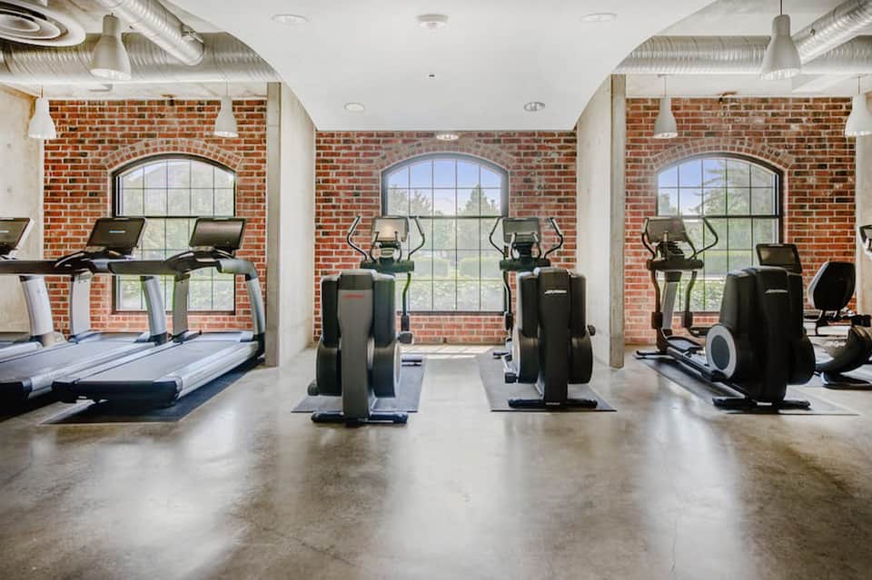 Fitness center with treadmills, ellipticals, and exercise equipment facing exposed brick walls