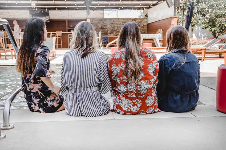 Four women sitting poolside overlooking outdoor lounge area and water
