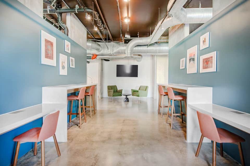Modern office break room with blue walls, colorful chairs, and TV screen