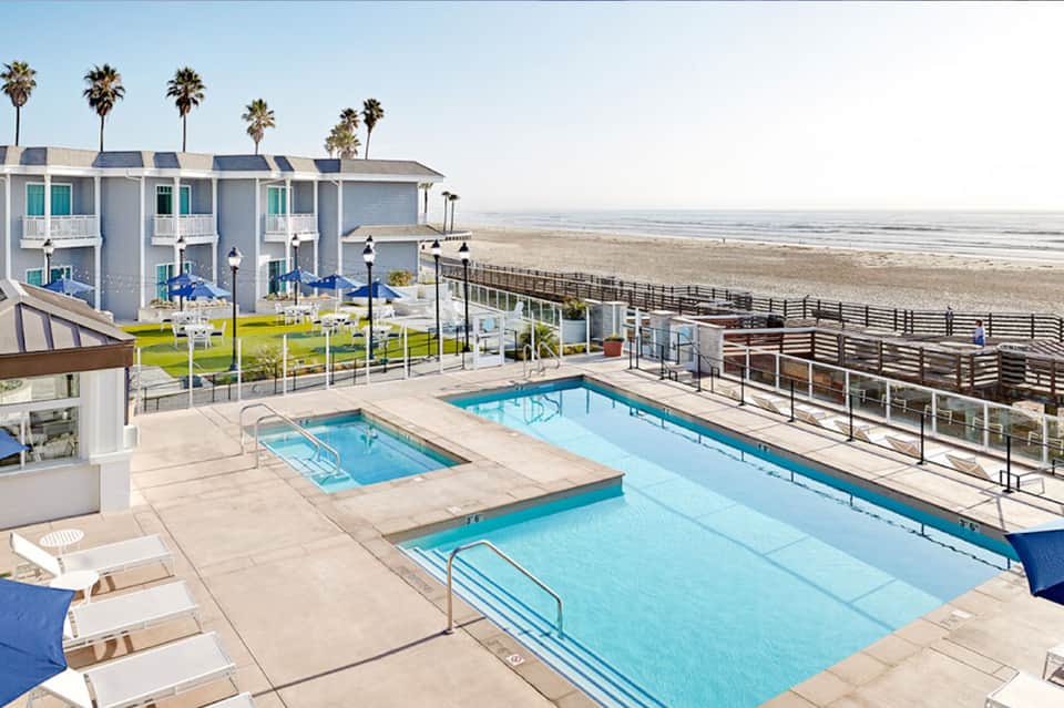 Beachfront pool area with two pools, lounge chairs, and ocean view with white beach cottages