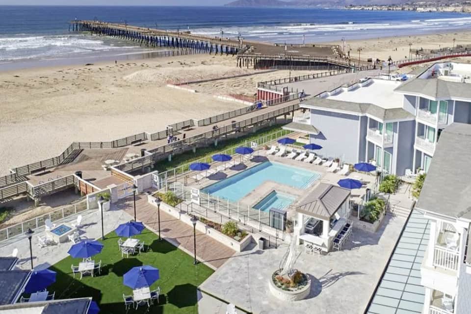 Beachfront resort with ocean view, pool, blue umbrellas, and pier