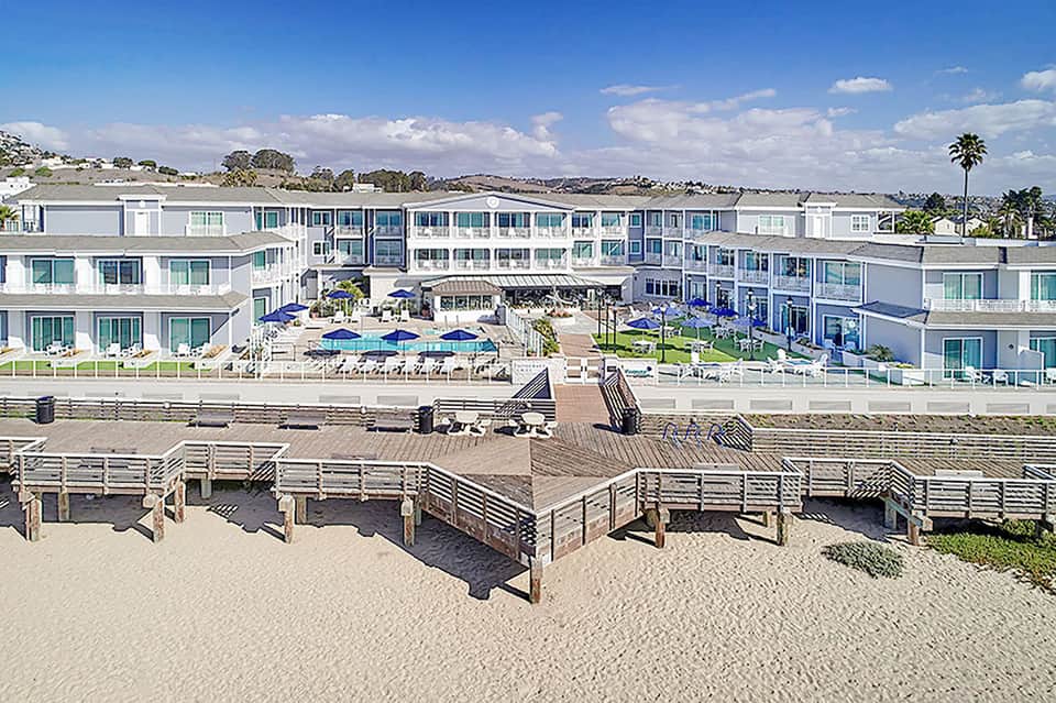 Modern beachfront resort with white architecture, blue umbrellas, and manicured grounds
