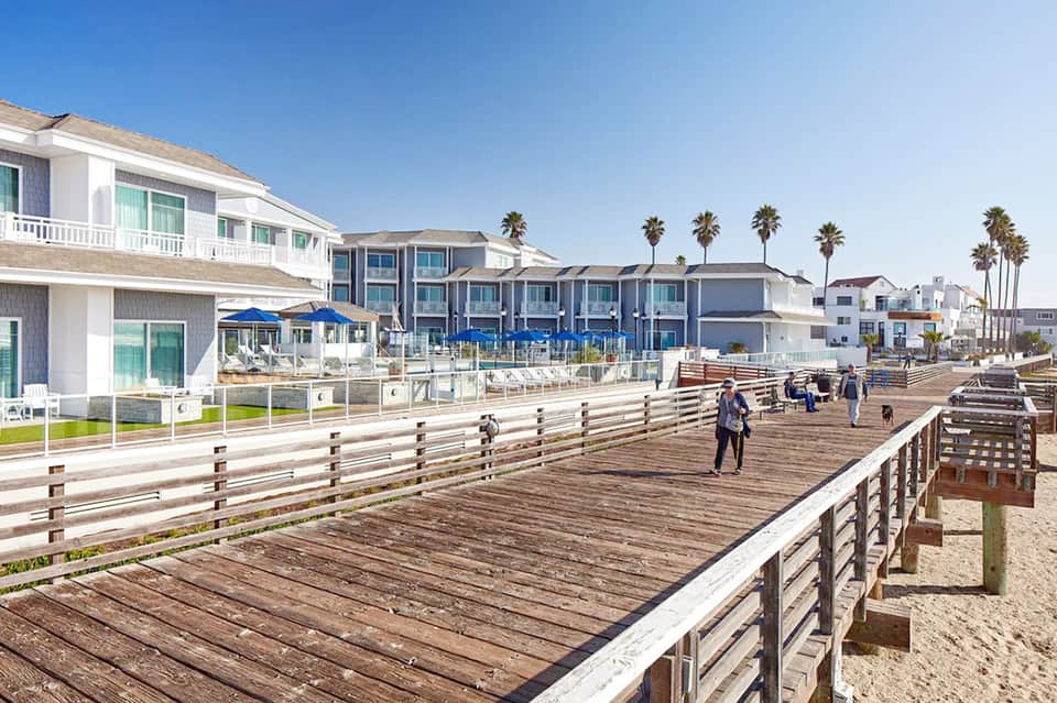 Beachfront boardwalk with coastal homes and palm trees under clear sky