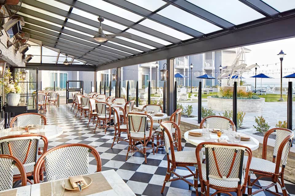 Modern covered patio dining area with checkered floor, woven chairs, and waterfront views