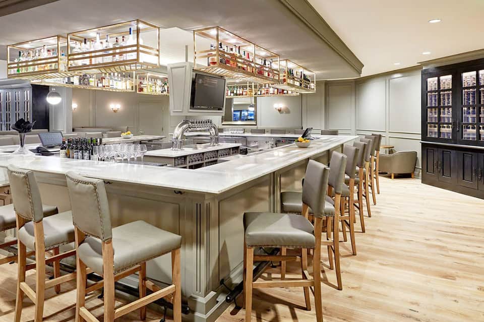 Upscale home bar with marble countertop, leather bar stools, glass shelving, and wine refrigerators