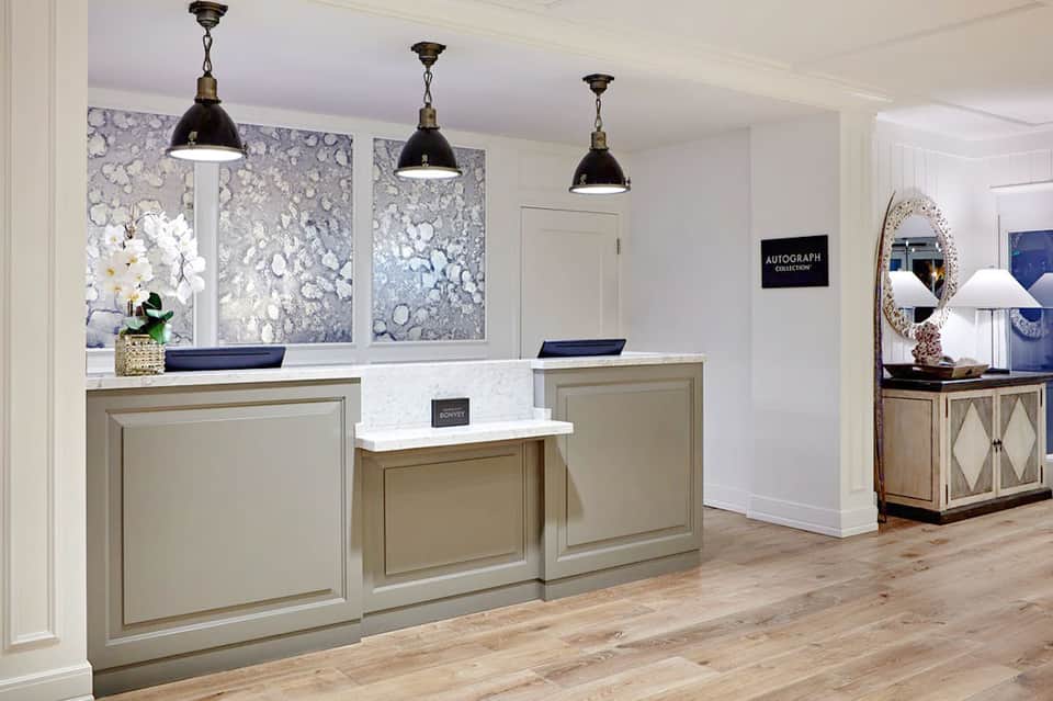 Modern hotel check-in desk with taupe cabinetry, pendant lights, and marble counters