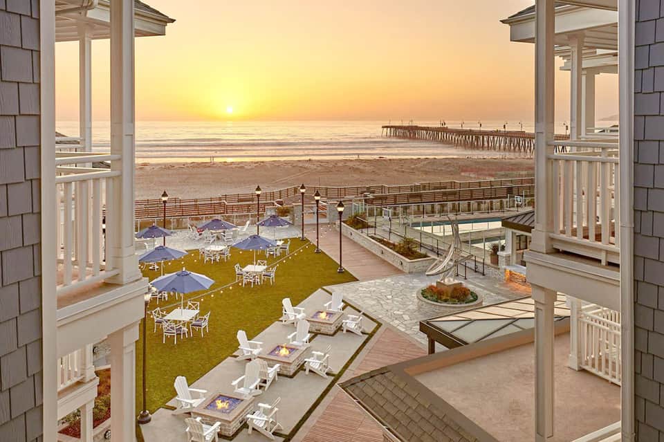Sunset beach view from elevated patio with umbrellas, lounge chairs, and pier in distance