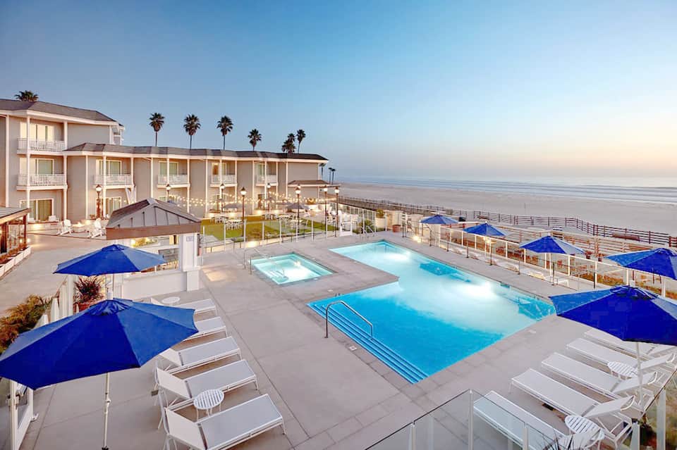 Beachfront resort with multiple pools, blue umbrellas, lounge chairs, and ocean view at dusk