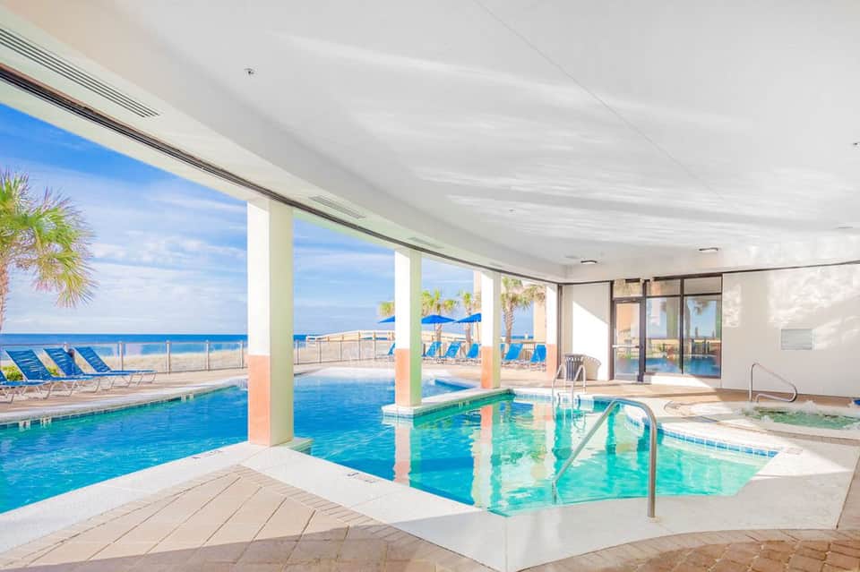 Indoor pool and hot tub facility with ocean view through large windows and beach beyond