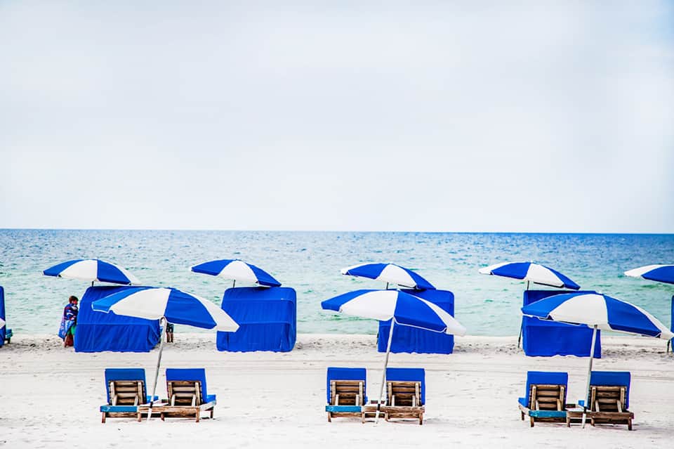 Beach scene with blue and white striped umbrellas and wooden lounge chairs lined on sand