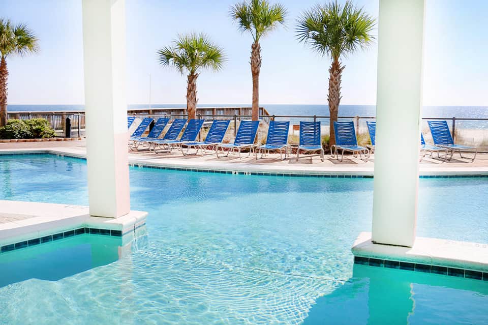 Indoor pool with blue lounge chairs, palm trees, and ocean view through columns