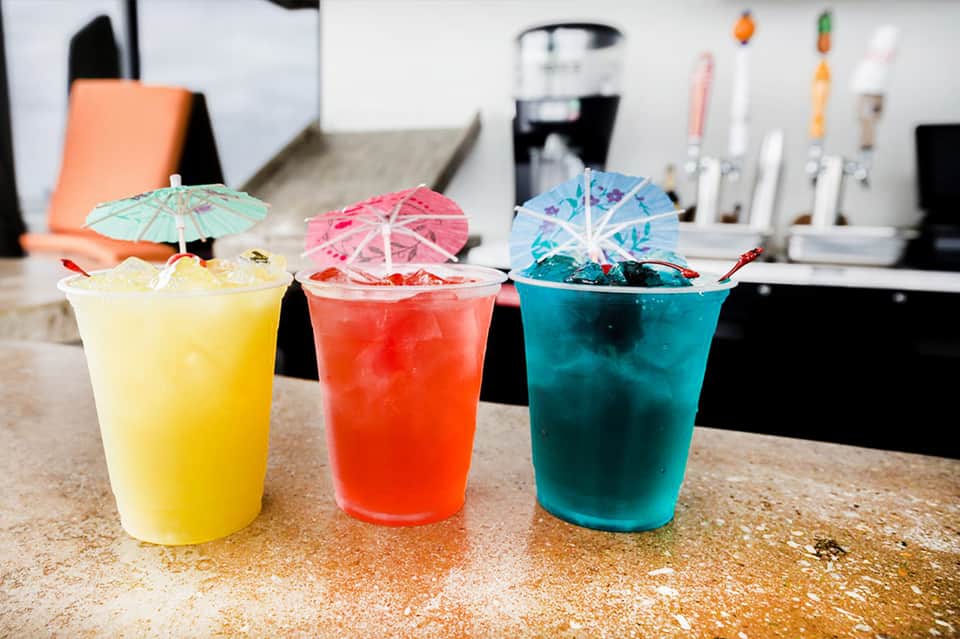 Three colorful tropical cocktails with decorative umbrellas on bar counter