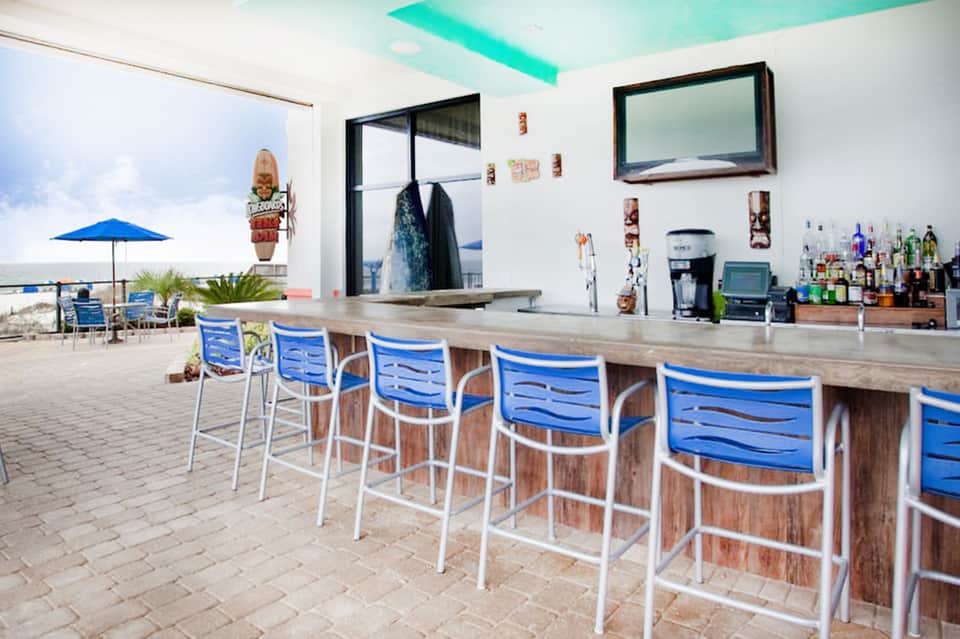 Beachfront bar with turquoise ceiling, blue bar seating, ocean view, and wooden counter