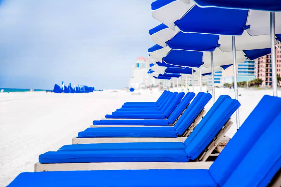 Row of blue beach lounge chairs with white umbrellas on sandy beach