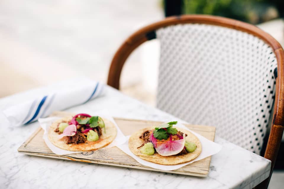 Two gourmet tacos with radish, cucumber, and cilantro on a marble table