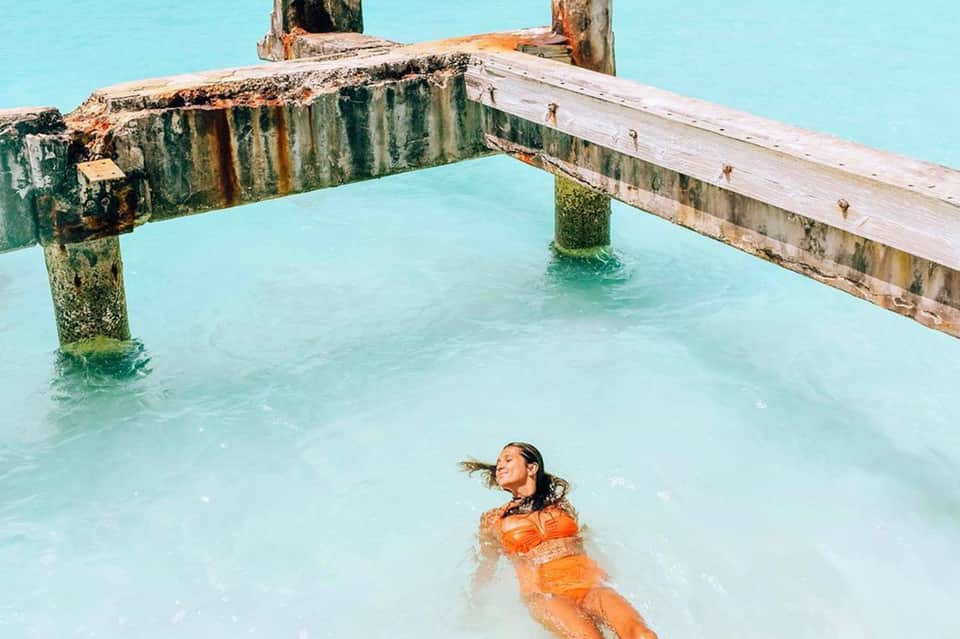 Woman swimming in turquoise water beneath weathered wooden pier structure