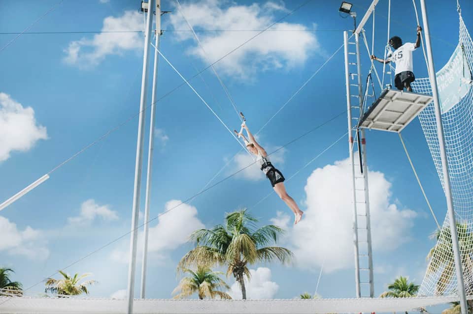 Guest on zip line adventure course suspended over resort grounds with palm trees visible