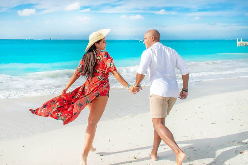 Couple holding hands walking on pristine white sand beach with turquoise water