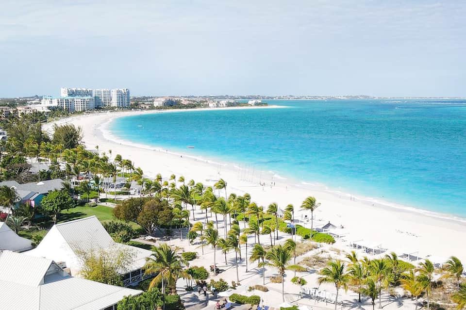 Beachfront resort with turquoise ocean, white sand beach, palm trees, and coastal hotel buildings