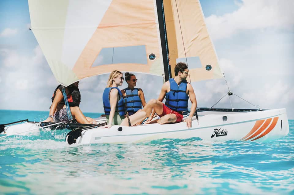 Three guests sailing on small white sailboat in turquoise tropical waters