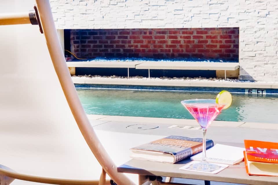 Pink cocktail with lime garnish on table beside swimming pool and modern architecture