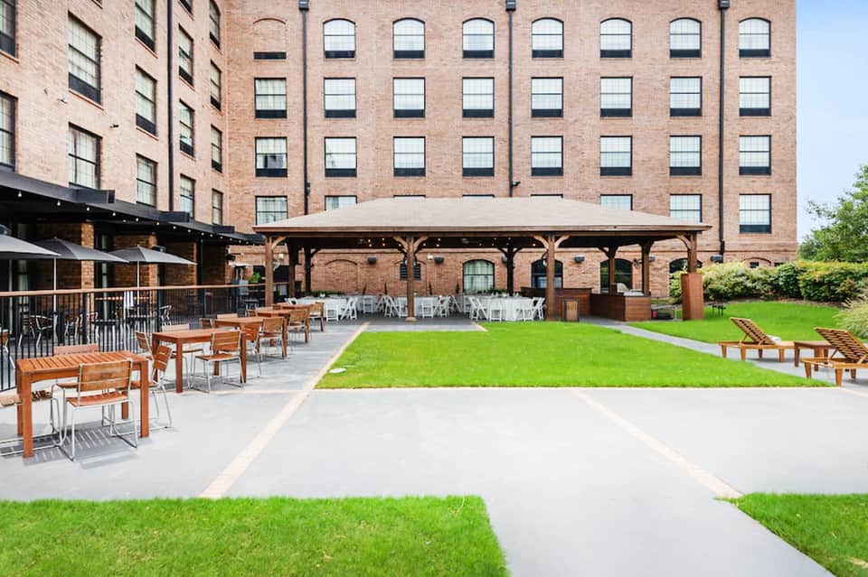 Modern courtyard with green lawn, wooden seating, pavilion, and brick buildings