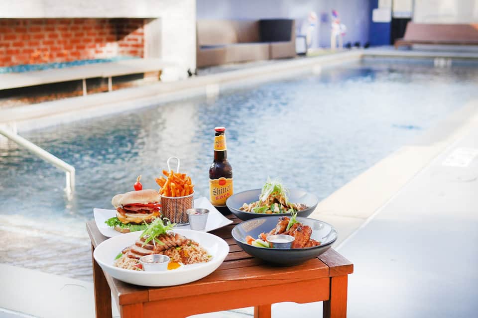 Poolside dining setup with burgers, salad, and beverages overlooking the water