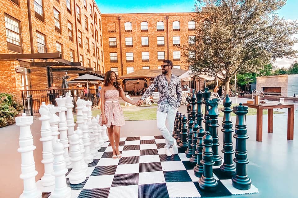 Couple playing giant chess on outdoor patio of urban resort with brick buildings