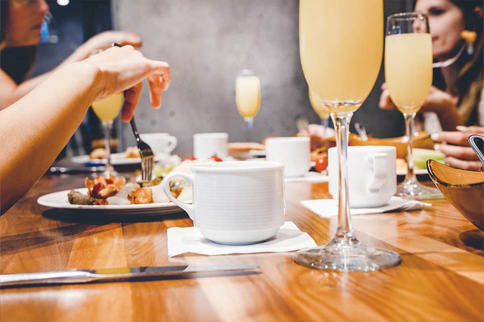 Guests toasting with champagne glasses during brunch service at wooden dining table