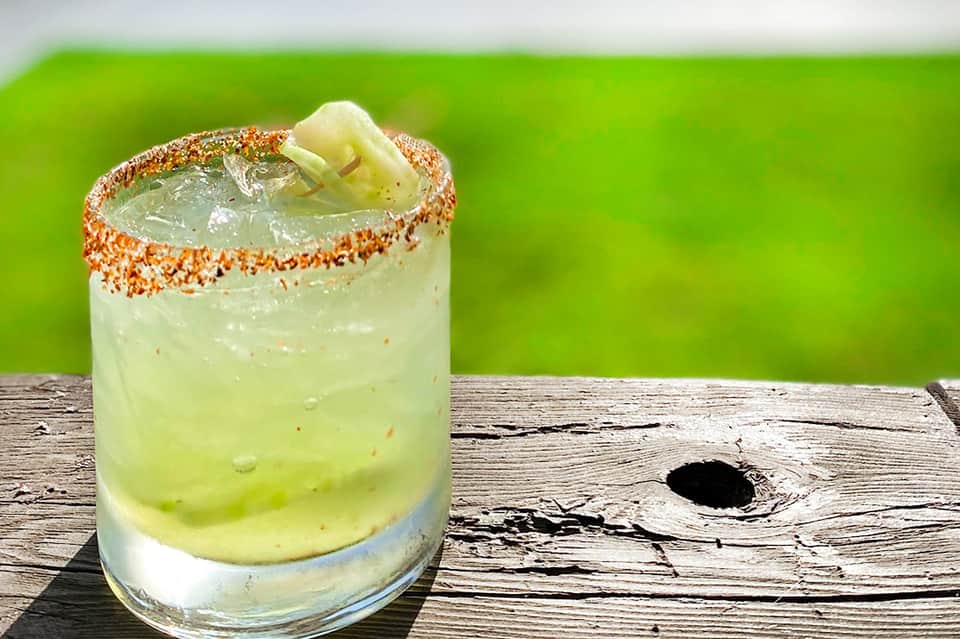 Margarita cocktail with salted rim and lime slice on wooden surface with green background