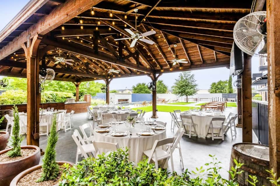 Wooden pavilion event space with rustic beams, string lights, round tables with white linens and green lawn