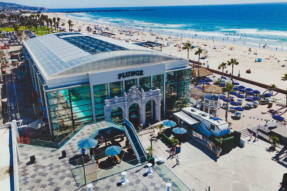 Modern beachfront facility with glass roof overlooking sandy beach with palm trees and blue umbrellas