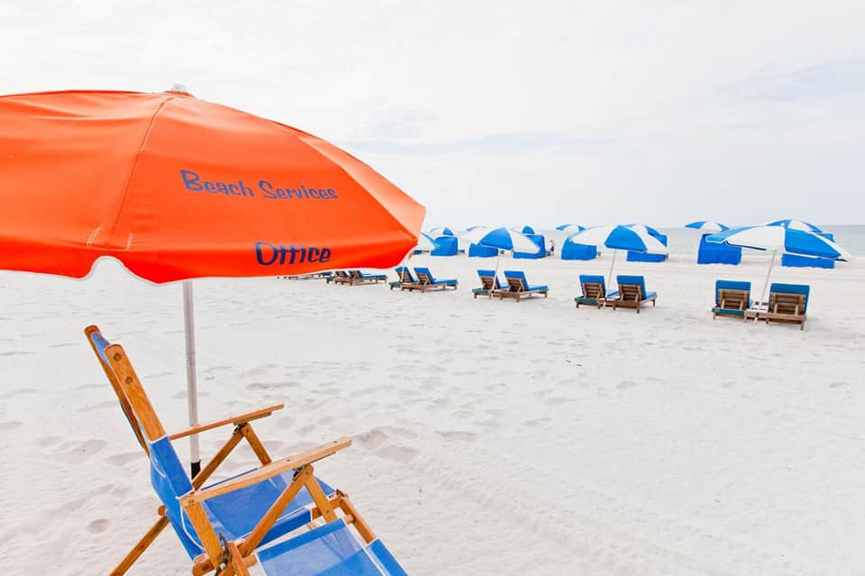 Beach service with red umbrella labeled 'Beach Services Office' and blue umbrellas with lounge chairs