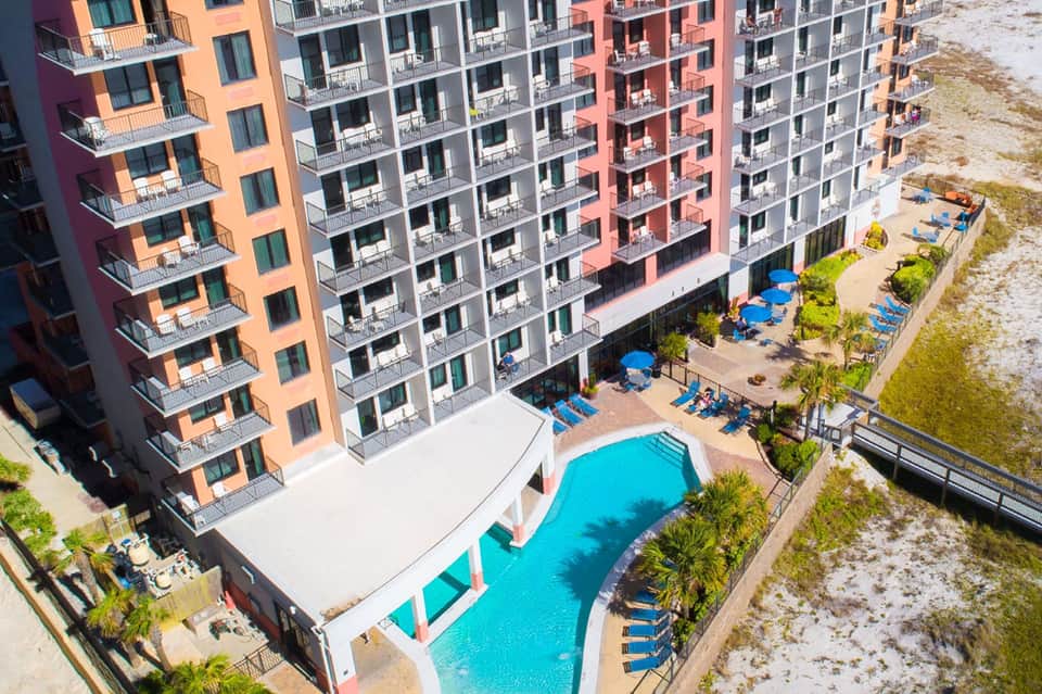 Aerial view of beachfront resort with colorful buildings, pool, and sandy beach access