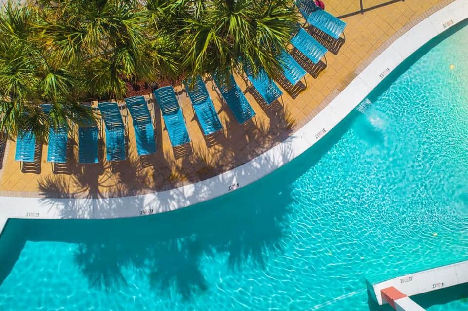 Resort pool with turquoise water, blue loungers under palm trees, and sandy yellow decking